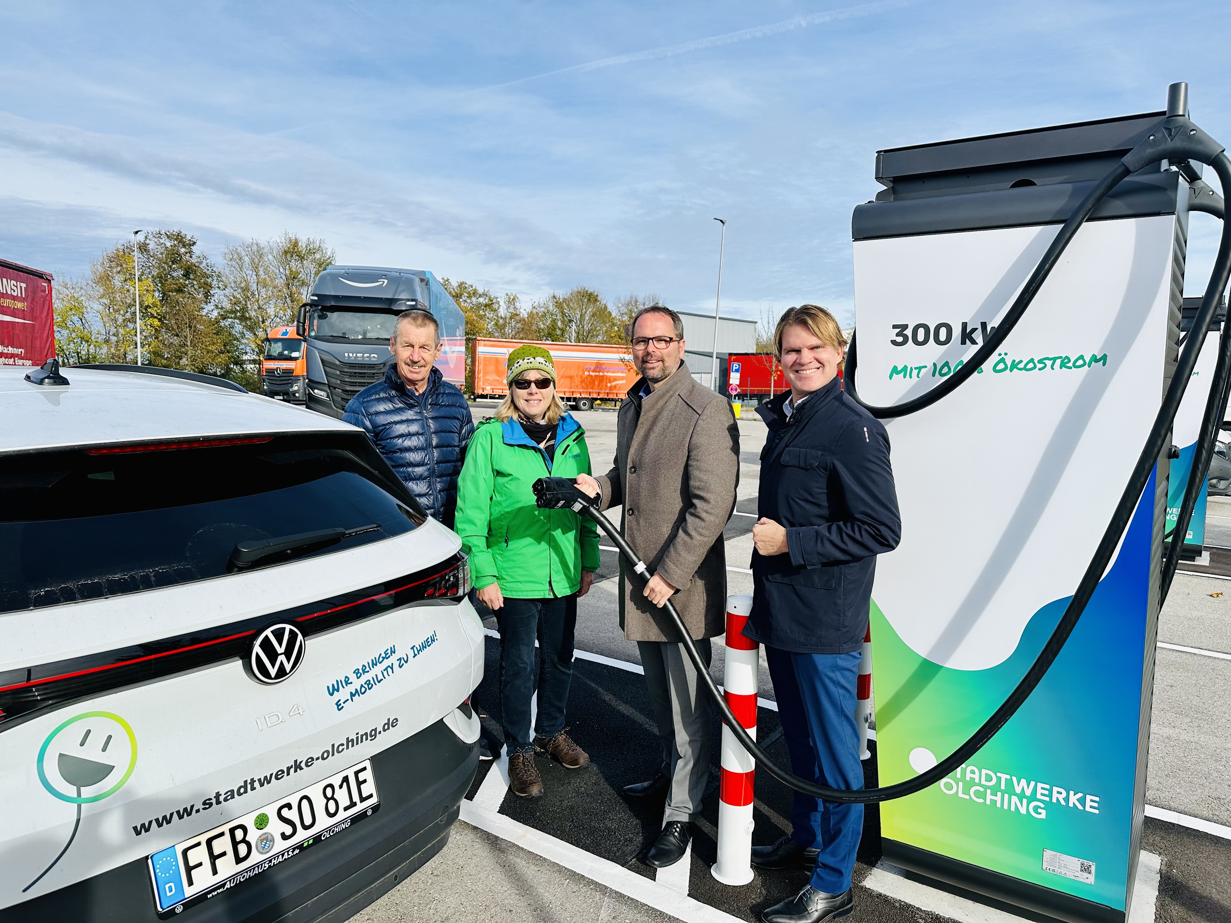 Andreas Magg und 3 andere Personen vor einem elekrtischen Auto. Im Hintergrund ist eine Elektrische Ladsäule von welcher Andreas Magg  den Stecker hält